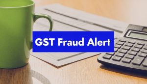 GST fraud alert banner displayed over a desk with a calculator, paperwork, and coffee mug.