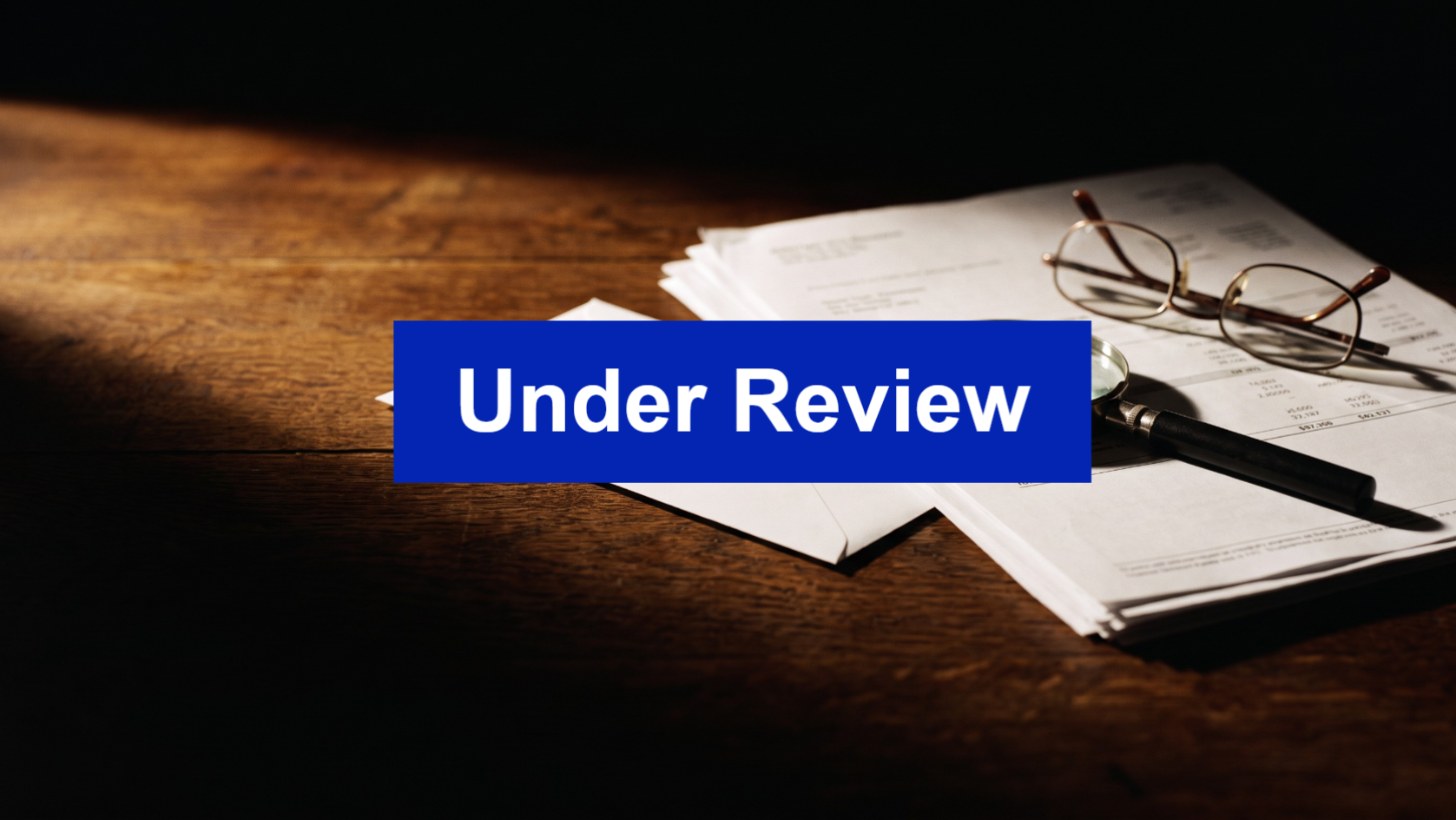 Envelope, tax documents and a magnifying glass on a desk with an Under Review banner, illustrating an ATO review of a tax return